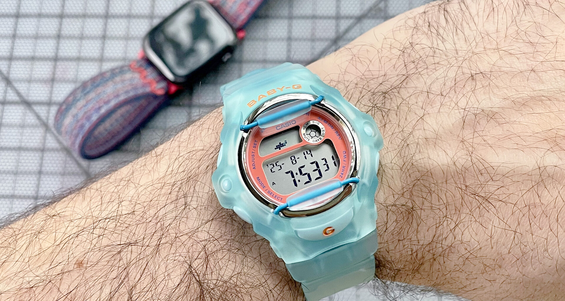 Close-up of the Casio Baby-G BG169 is semitransparent baby blue on the writer's wrist with an Apple Watch 10 out of focus in the background