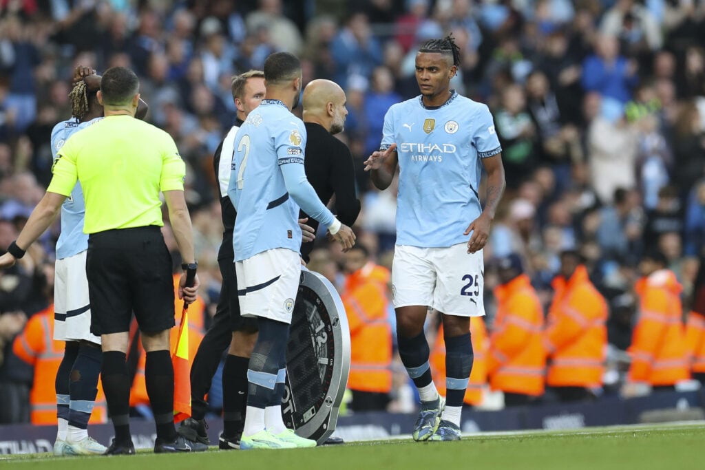 Manuel Akanji interacting with Pep Guardiola on the touchline during a Man City game, while Kyle Walker waits to enter the pitch