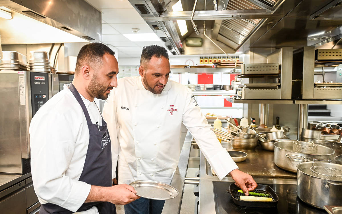 Michael Caines and another chef in a kitchen both watching an ingredient cooking in a pan