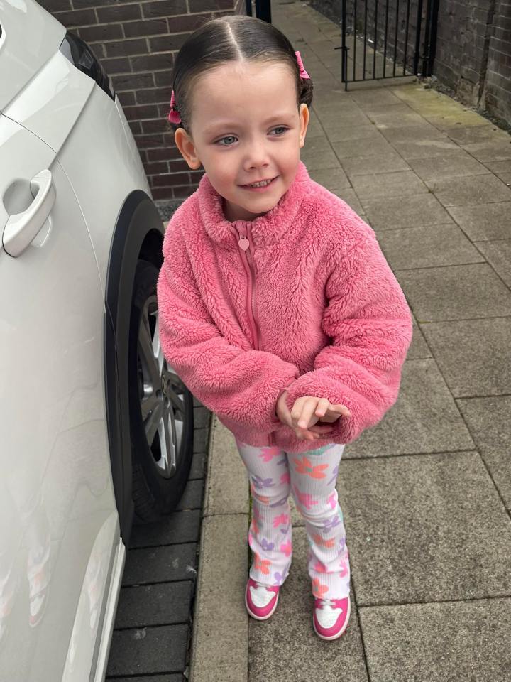 Young girl in pink jacket and floral pants.