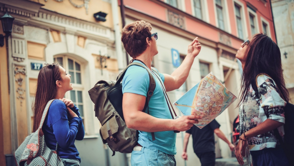 A group of people with bags and backpacks holding a map while looking at a building.