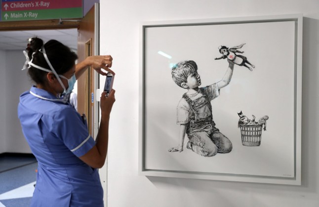 A member of staff takes a photograph of the new artwork painted by Banksy during lockdown, entitled 'Game Changer', which has gone on display to staff and patients on Level C of Southampton General Hospital. PA Photo. Picture date: Thursday May 7, 2020. See PA story ARTS Banksy. Photo credit should read: Andrew Matthews/PA Wire