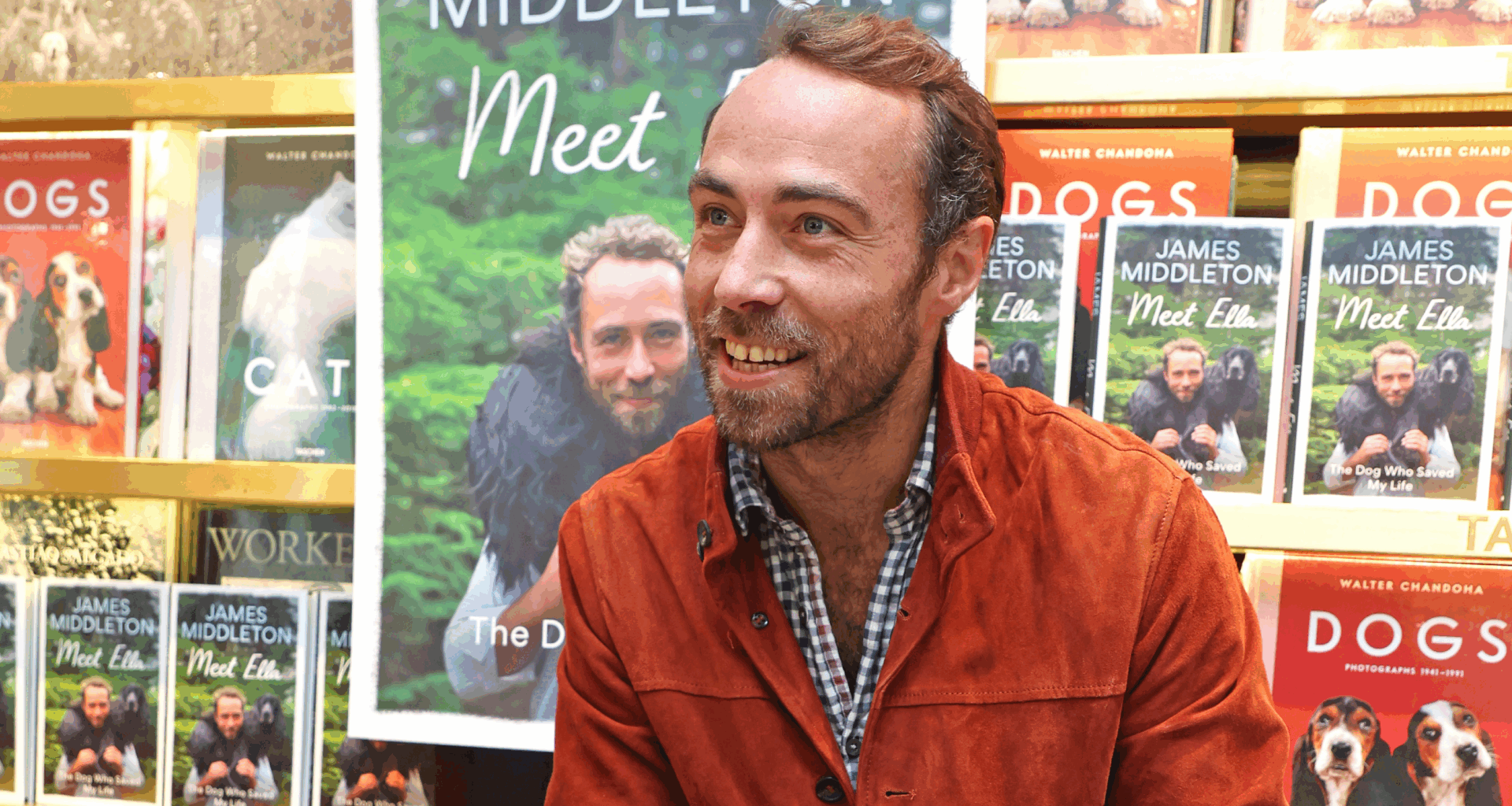 James Middleton sitting in front of a table of his memoir and bookshelves with dog books