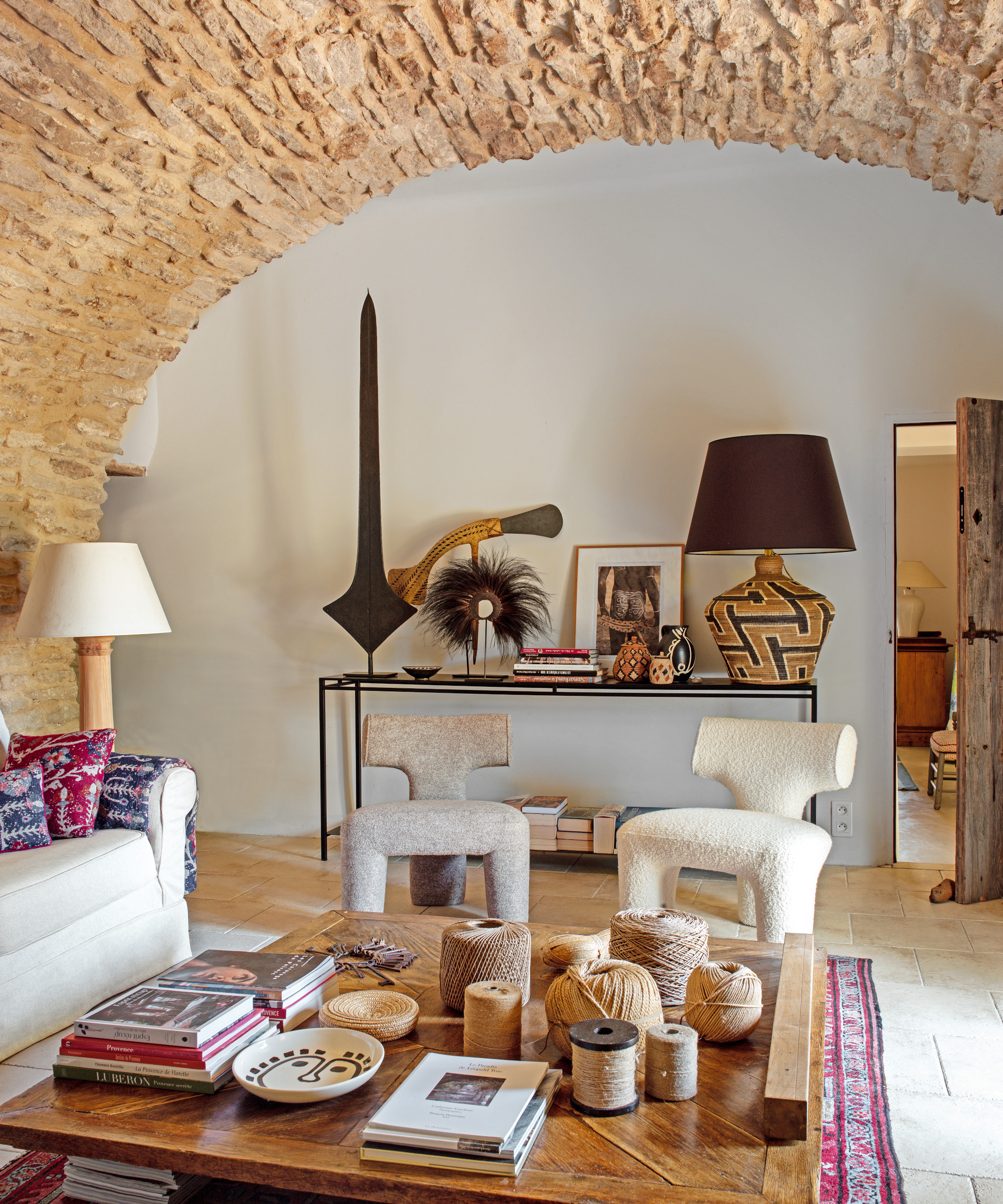 vaulted living room with thick stone arch, white sofa, modern chairs, wooden coffee table and South African objects
