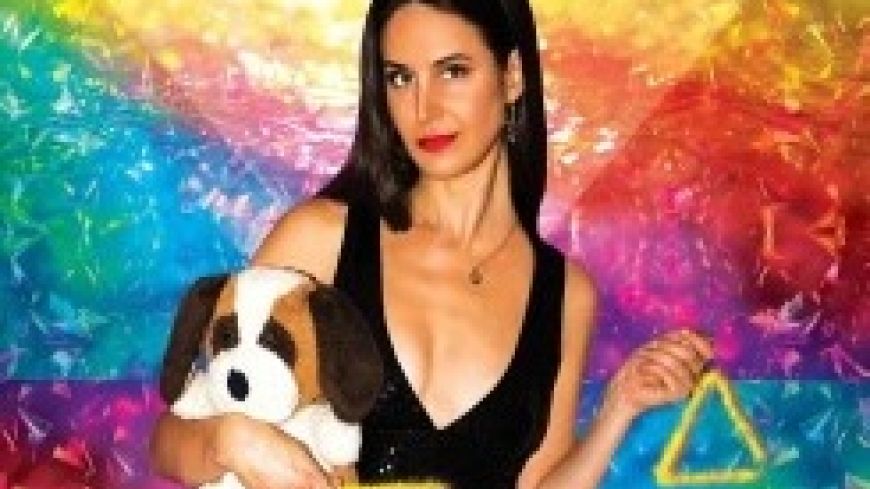 Brooke in a black top and trousers, holding a toy dog, with a rainbow coloured background.