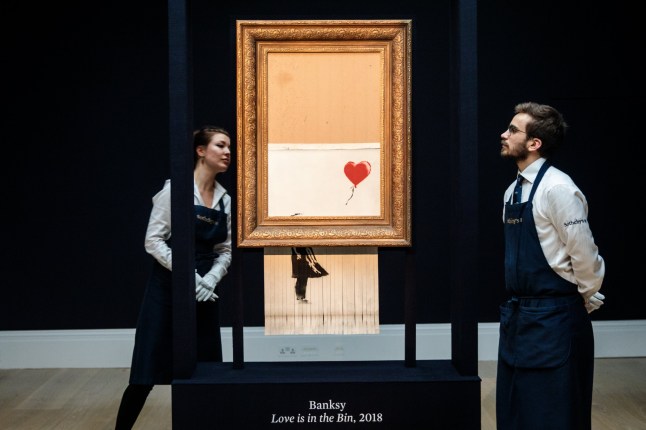 LONDON, ENGLAND - OCTOBER 12: Sotheby's employees view 'Love is in the Bin' by British artist Banksy during a media preview at Sotheby's auction house on October 12, 2018 in London, United Kingdom. During Sotheby's Contemporary Art Sale on 5th October the Banksy artwork 'Girl with Balloon' shredded through the bottom of the frame as it was sold. With Banksy being responsible for the shredding, the buyer has agreed to proceed with the sale and it is now titled 'Love is in the Bin' and said to be worth more than the ??1.04million paid. (Photo by Jack Taylor/Getty Images)