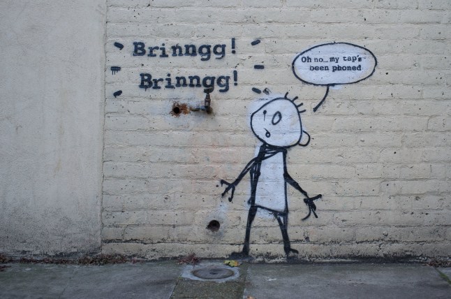 Banksys Phone Tap, known as My Taps Been Phoned is seen in East London on August 13, 2017. For this stunt, Banksy tagged a wall with a playful and light-hearted take on Rupert Murdochs phone hacking scandal, wading into the debate embroiling News International. It depicts a water tap (a real tap found on the wall and incorporated in the artwork) with a simulated phone ringing and a confused stick figure person. (Photo by Alberto Pezzali/NurPhoto via Getty Images)