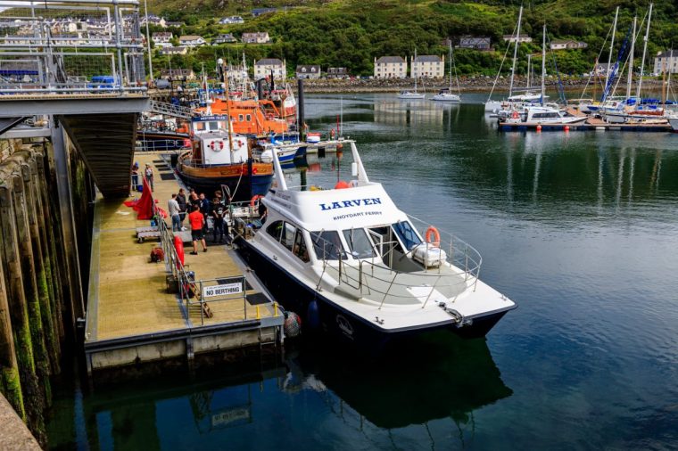 Twin hulled passenger ferry, the Larven, the Knoydart ferry at Mallaig docks with passengers waiting to board. At the Ferry port of Mallaig, Lochaber, Inverness-shire with multiple shipping vessels, yachts and trawlers in the background.