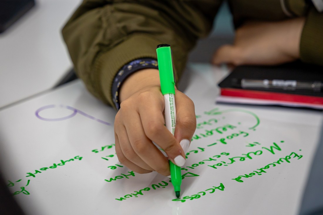 A student with white fingernail polish writes notes with a bright green marker.