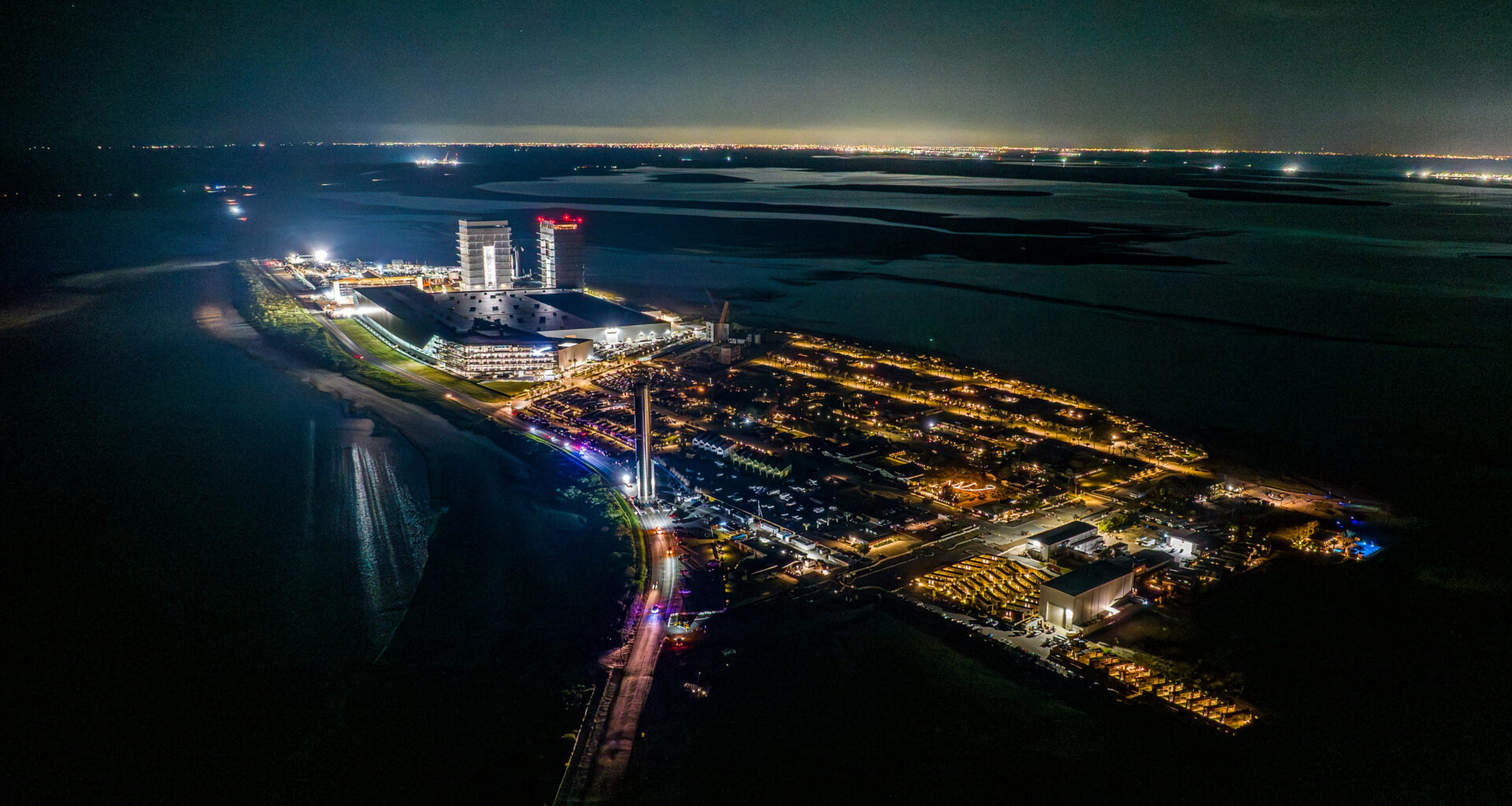 overhead view of a giant silver rocket rolling down a lit-up peninsula at night