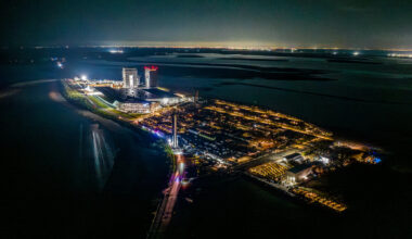 overhead view of a giant silver rocket rolling down a lit-up peninsula at night