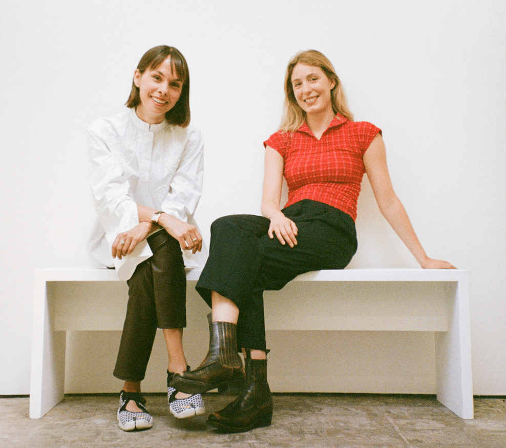 Two smiling women sit on a bench.