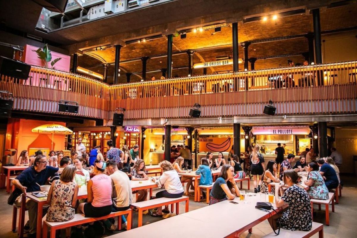 the bottom floor of seven dials market, with people sat at long pink tables enjoying street food dishes and drinks
