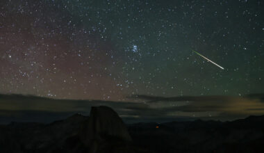 A bright meteor is pictured streaking across a starry night sky over a rocky landscape, as clouds lie low on the horizon.