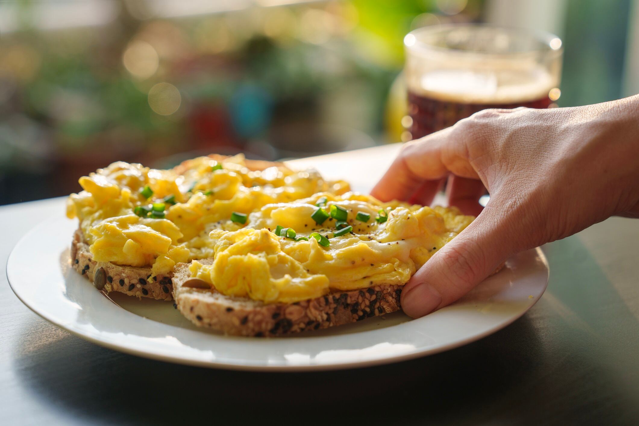Image of woman's hand holding a piece of toasted bread with scrambled eggs on top.
