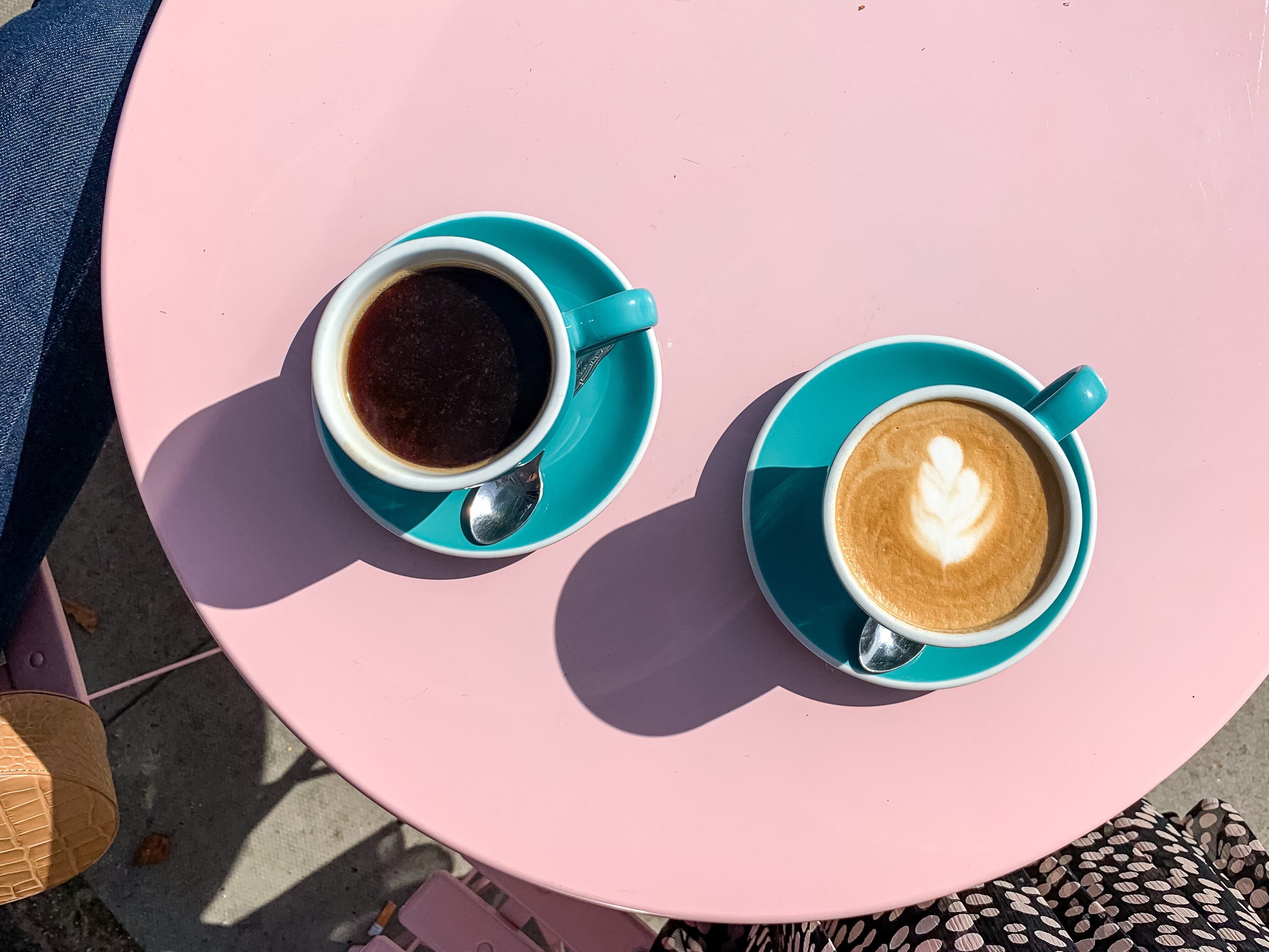 Morning coffees in tiffany color ceramic mugs with saucers on pink table. Black americano and latte. View from above