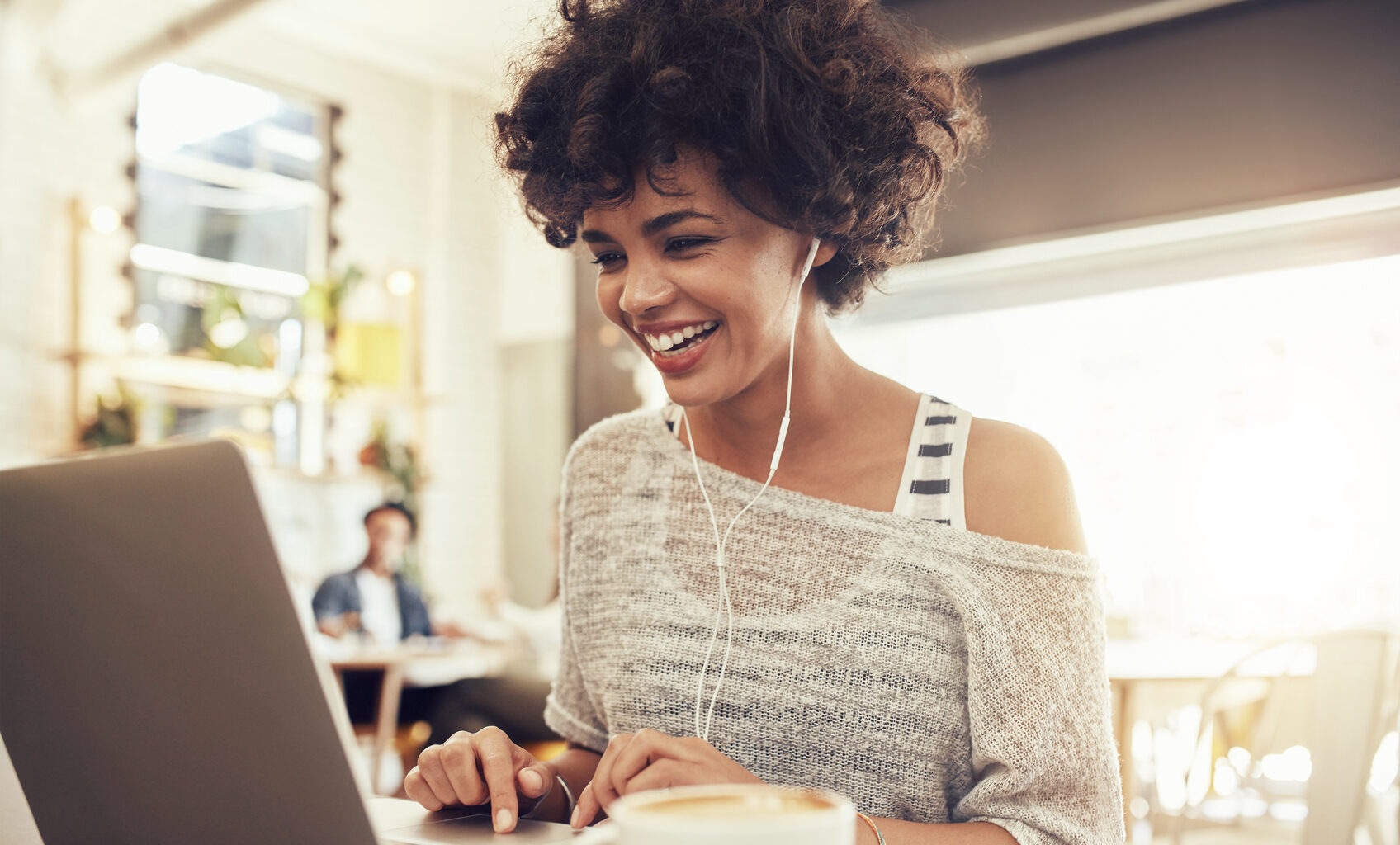 Image of happy woman using laptop while sitting at cafe. Young african american woman sitting in a coffee shop and working on laptop.