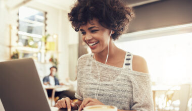 Image of happy woman using laptop while sitting at cafe. Young african american woman sitting in a coffee shop and working on laptop.