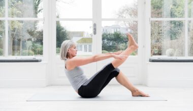 Woman in her 60s with grey bobbed hair stretching leg at home in front of windows overlooking a garden.