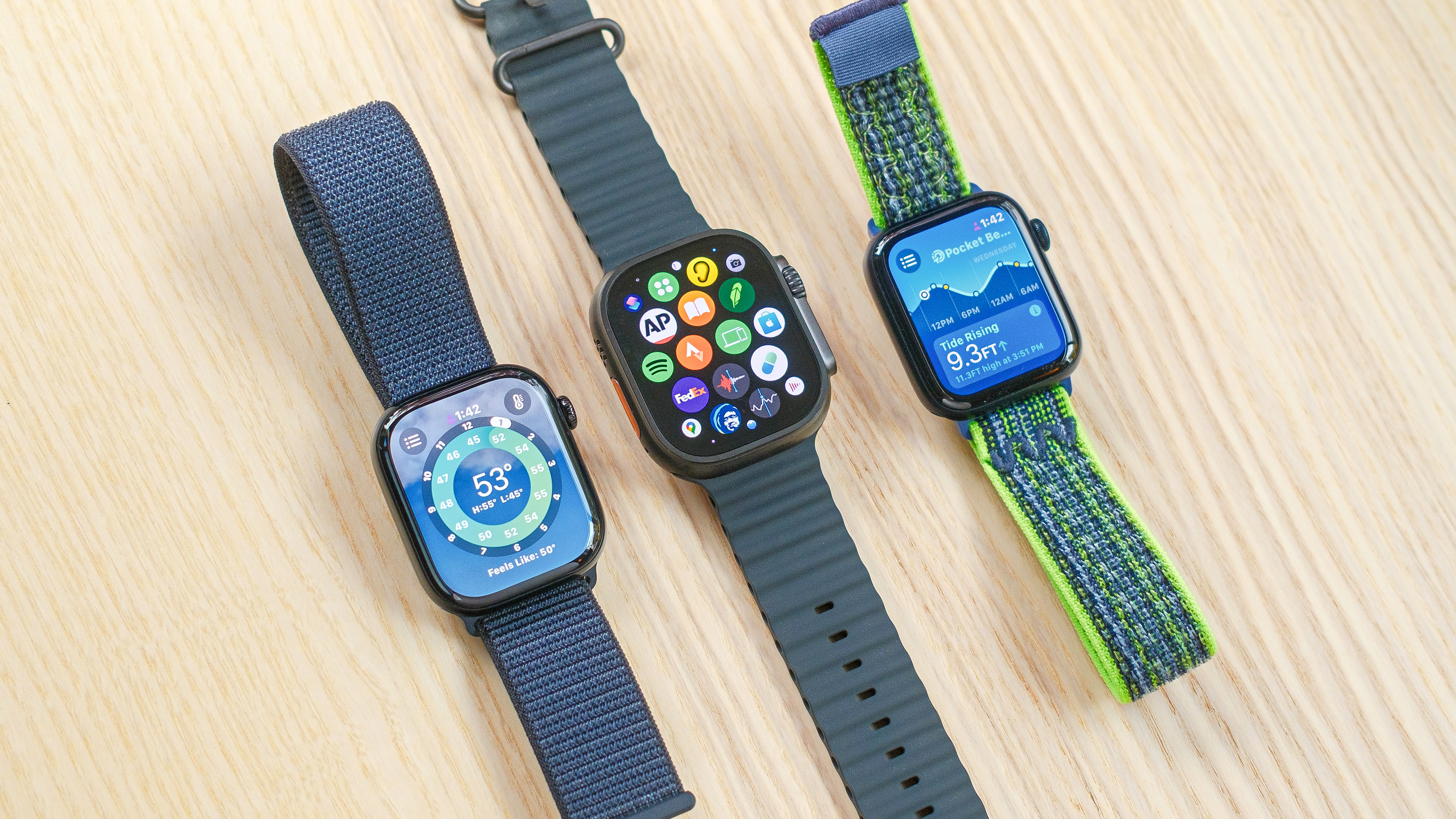 The Apple Watch Series 10, Apple Watch SE and Apple Watch Ultra 2 sitting next to each other on a wooden table