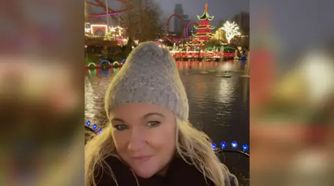 Justine Tipling Justine Tipling. She has long blonde hair and is wearing a grey beanie. She is pictured at night in Tivoli Gardens in Copenhagen, Denmark, standing in front of a pond. The rides and park are lit up behind her. She is looking directly at the camera and smiling.