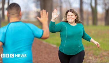 A woman runner gives a man a high five as she jogs past him in the park