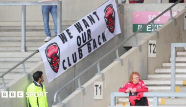 A Salford Red Devils banner displaying the message "we want our club back" at a Super League fixture against Wigan Warriors this season