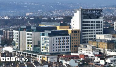An aerial photograph of a building made of three multi-coloured arms with a tower to the right of it.