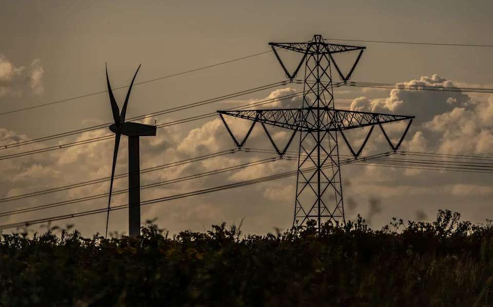 BATH, UNITED KINGDOM - JULY 16: A wind turbine generates electricity besides electrical pylons carrying electricity cables across fields on July 16, 2023 near Bath, England. The UK government has published documents with plans for Britain should it have to go ‘lights out’ this winter after the National Grid warned there could be blackouts due to the ongoing energy crisis. There are fears that Russian President Vladimir Putin will restrict gas supplies to Europe and although the UK does not rely on Russian energy supply, it does import from electricity and gas from European countries that do. With many consumers already facing a cost of living crisis with sharp rises in their home energy bills, energy blackouts look set to compound their misery this winter. (Photo by Matt Cardy/Getty Images)