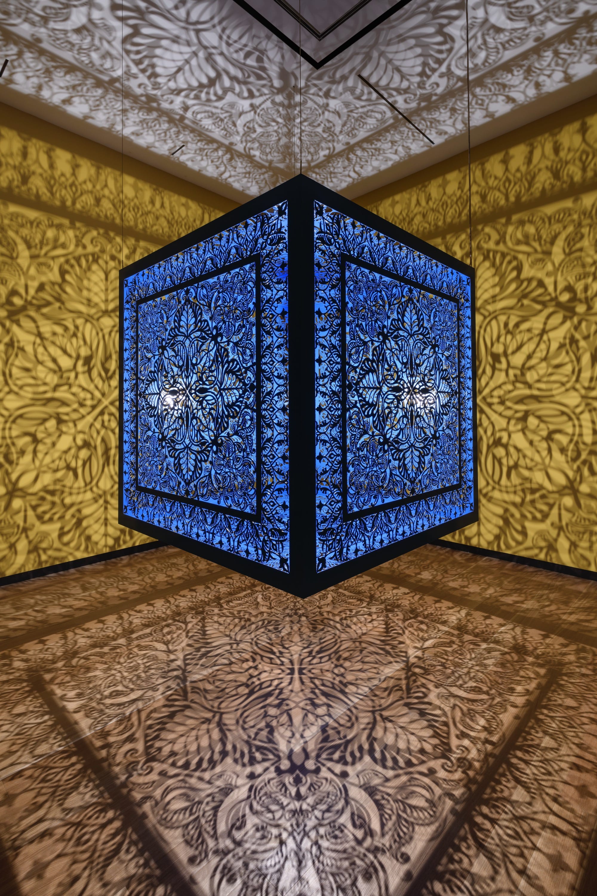 a sculptural installation in a yellow room, with light emitting from within a structure that casts ornate shadows onto the walls