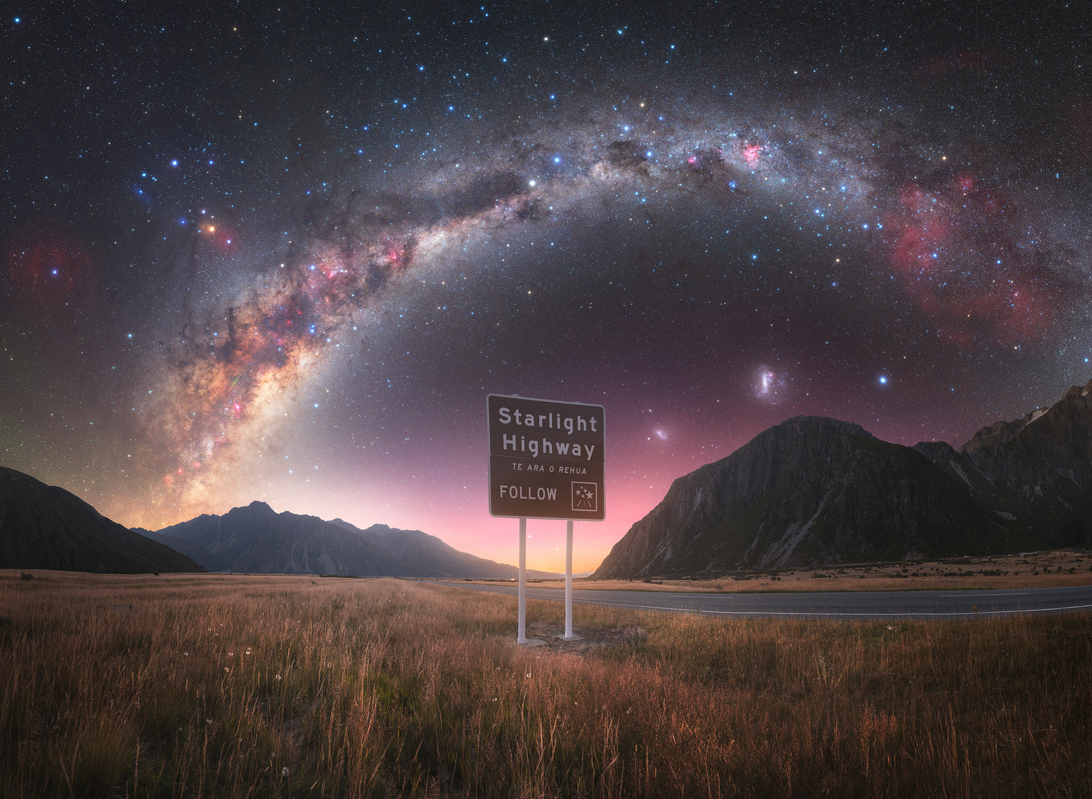 A sign for "Starlight Highway" against a breathtaking backdrop of the Milky Way and mountains at twilight