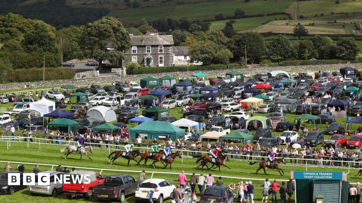 Cartmel Racecourse pictured during the Hadwins Motor Group Handicap Hurdle race in 2017. Horses are racing and the course is surrounded by cars and gazebos.