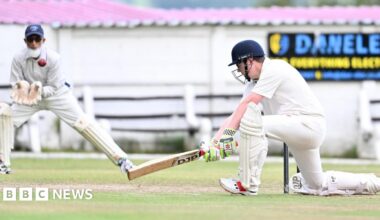 A vicar drives a ball with a wicket-keeping imam in the background