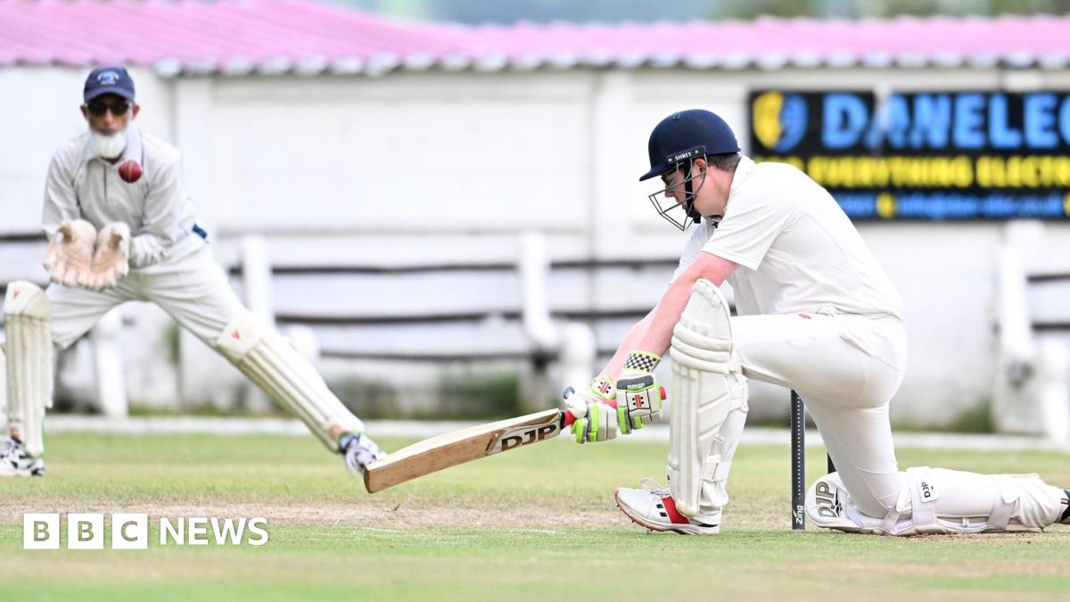 A vicar drives a ball with a wicket-keeping imam in the background