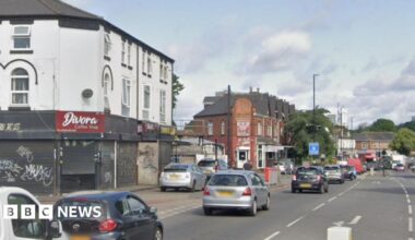 The junction of Ladypool Road and Stratford Road in Birmingham. The daytime photograph shows cars queueing in the city and road markings for a junction, with a bollard just visible. There are shops and other businesses along the road.