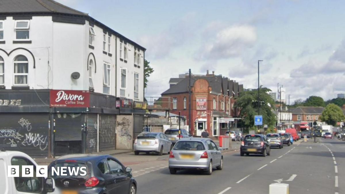 The junction of Ladypool Road and Stratford Road in Birmingham. The daytime photograph shows cars queueing in the city and road markings for a junction, with a bollard just visible. There are shops and other businesses along the road.