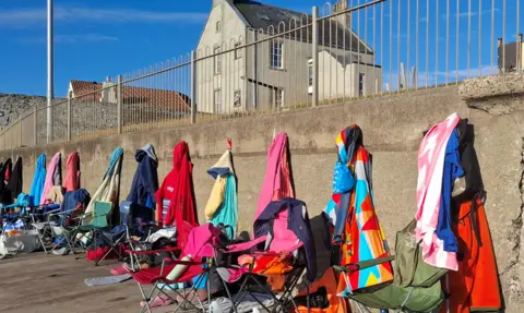 Aileen McFarlane A row of brightly-coloured towels and robes hang along the beach wall like a rainbow at Cellardyke Tidal Pool, camp chairs on the beach also hold swimmers' things.
