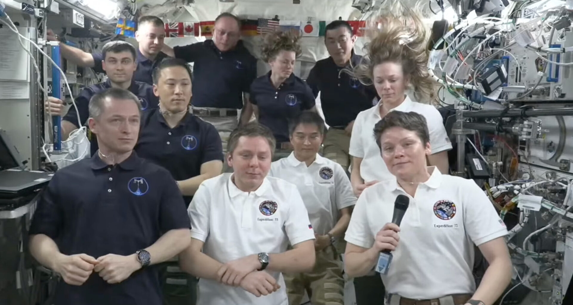 11 people stand in a cramped space station module during a farewell ceremony
