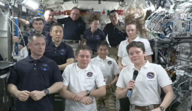 11 people stand in a cramped space station module during a farewell ceremony