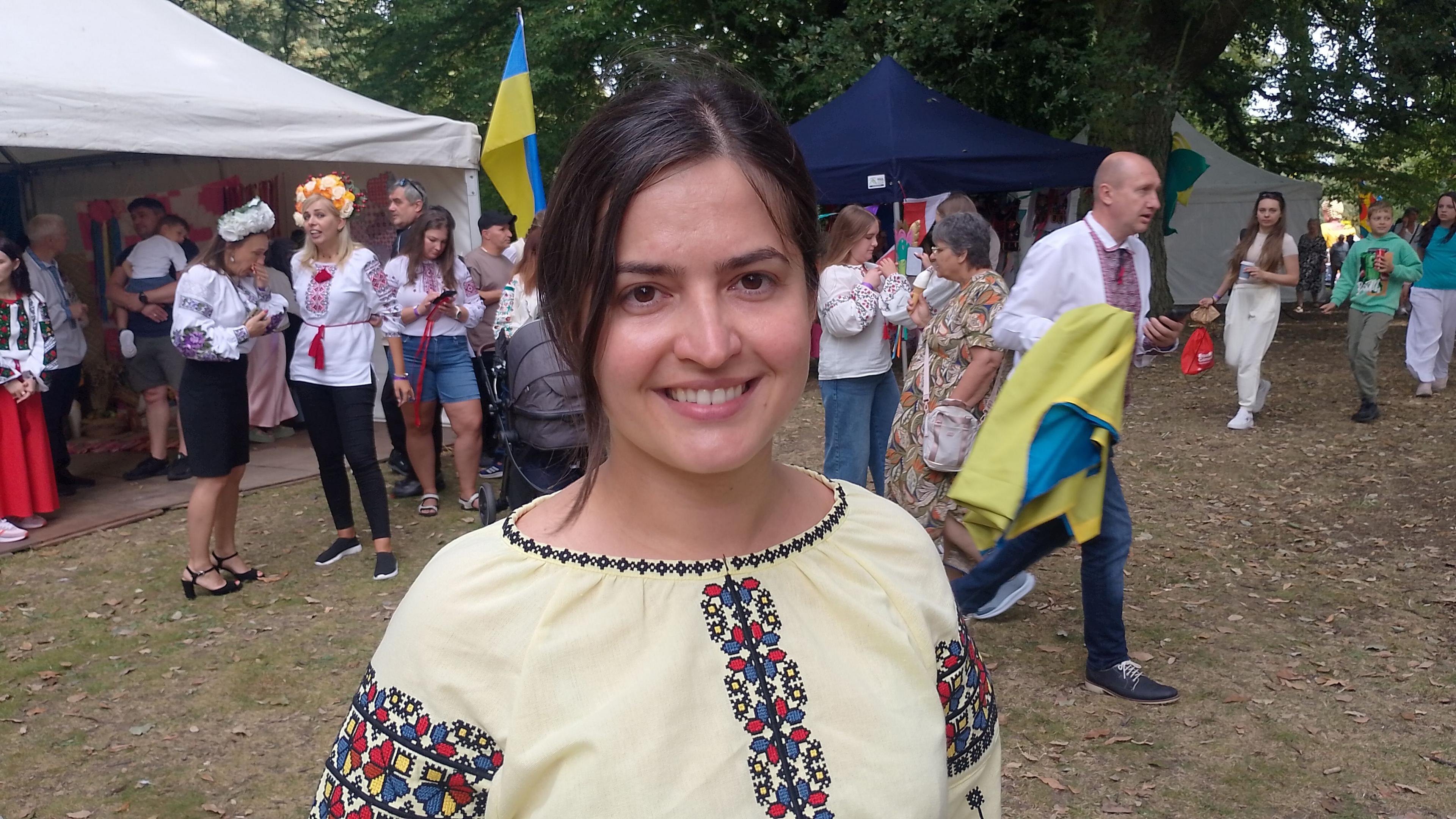 A brunette woman smiles at the camera. She wears a cream embroidered top. 