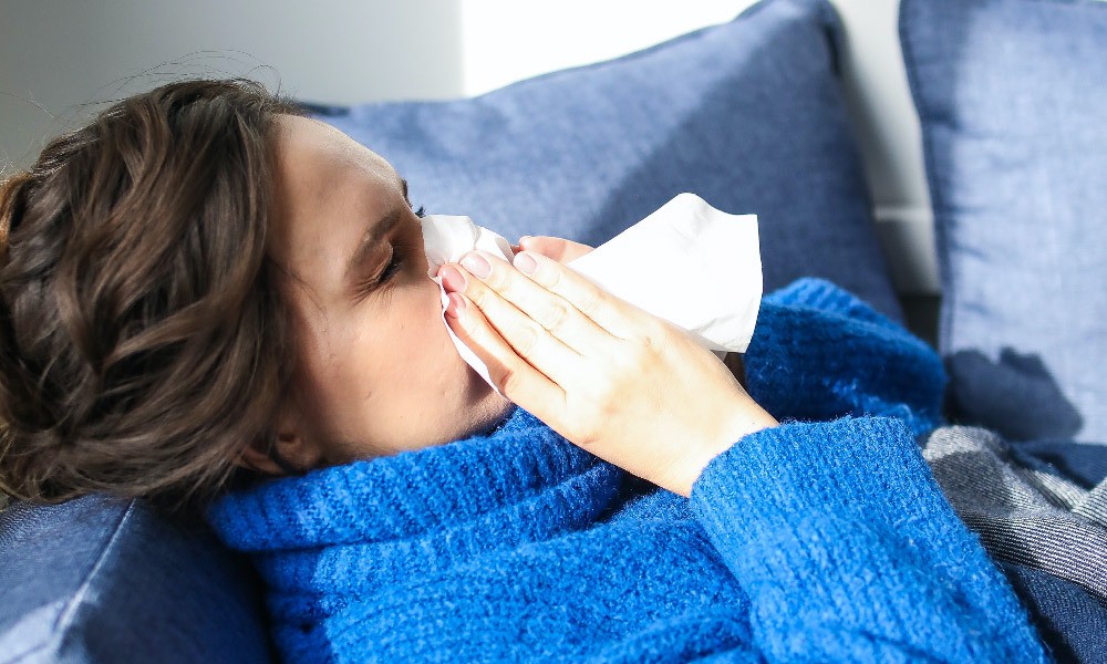 A woman lying on her sofa blows her nose.