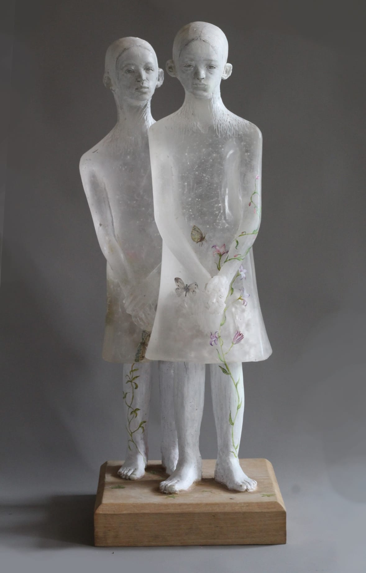 glass sculpture of two young figures, one standing in front of the other