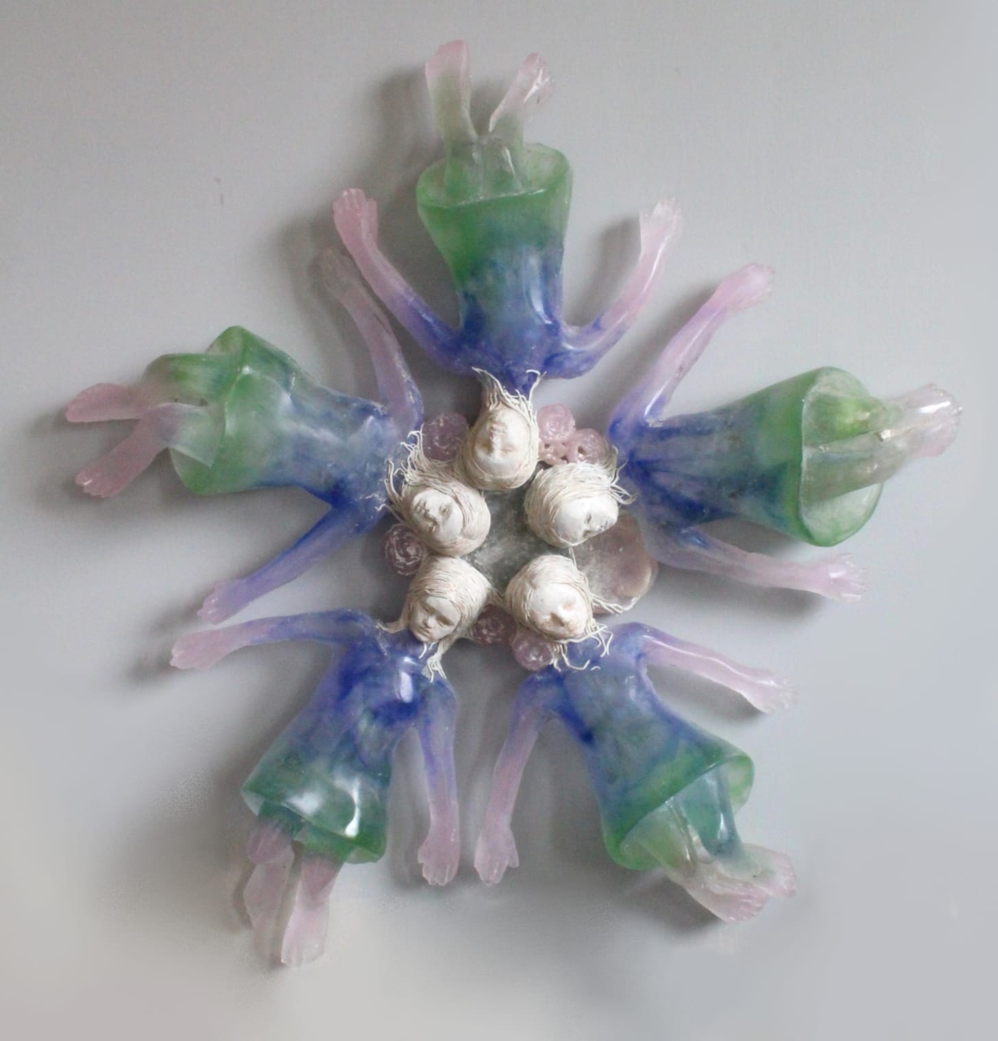 a glass and ceramic sculpture of five girls all laying in a circle with their heads together and bodies outstretched, like a star
