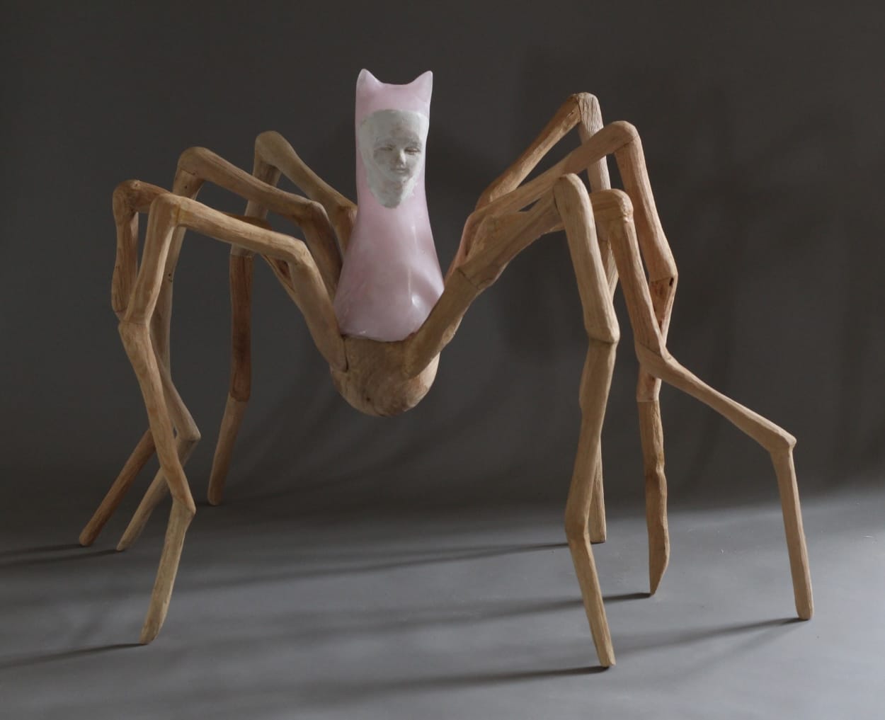 a glass sculpture of a young figure in a pink cat costume, with spider-like wooden legs