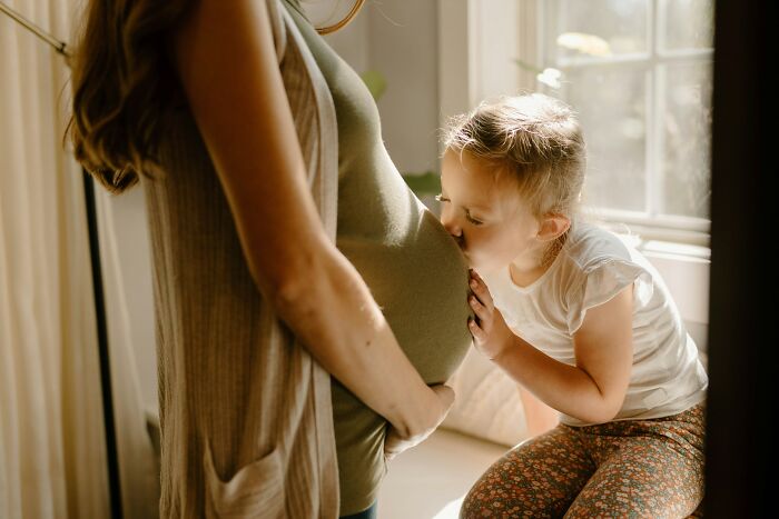 Young child kissing pregnant woman’s belly showing cool facts about the human body and family connection.