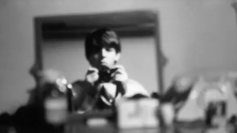 Paul McCartney, Courtesy Gagosian Titled: Self-portrait in my room at the Asher family home, Wimpole Street, London, December 1963. A black and white, out of focus image of Paul McCartney holding his camera in both hands, and pointed at a mirror. He has a straight face and does not smile. 