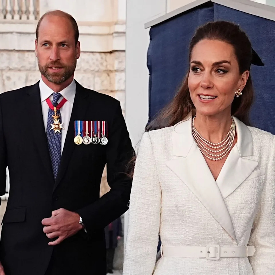  Prince William wears a suit and military medals and Kate Middleton wears a cream coat dress with a floppy black bow. 