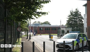 A police car is behind black bollards close to the car park where a 19-year-old was killed.