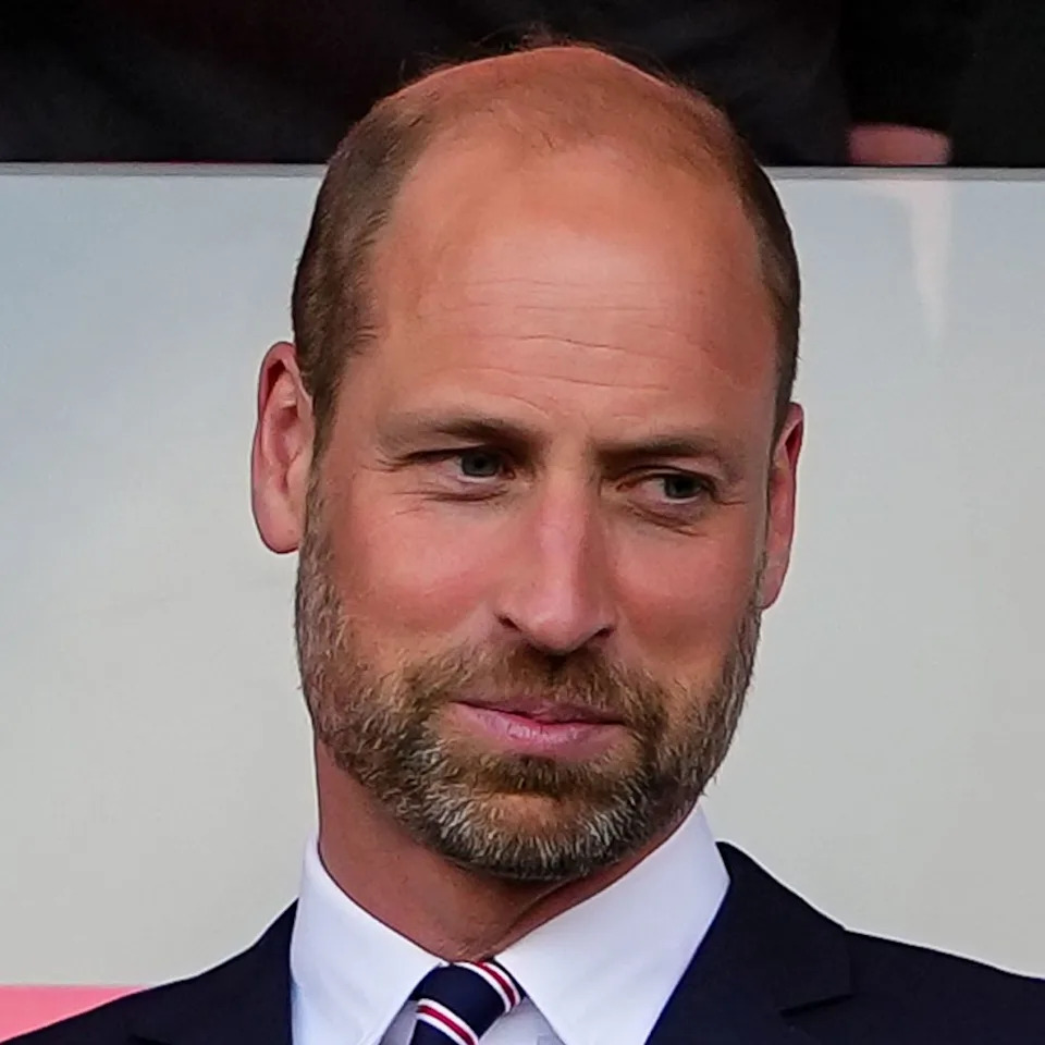  Prince William wearing a suit and tie in front of a pink and white background. 