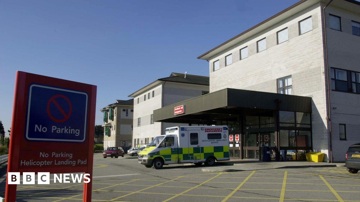 An ambulance is parked outside the entrance of a hospital building. A red no parking sign is on display, it says no parking, helicopter landing pad. The hospital building is grey.